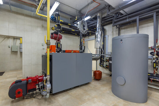 An industrial heating system inside a commercial building. There are pipes, a large tank, and machinery arranged in an organized manner. The equipment is functioning and well-maintained