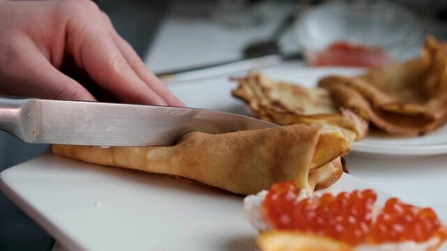 red caviar cut in half with a knifecut in half with a knife Thin tasty colorful pancakes. Close-up view of red, yellow and green cutaway rolled pancakes with cream cheese and salmon filling on a dish