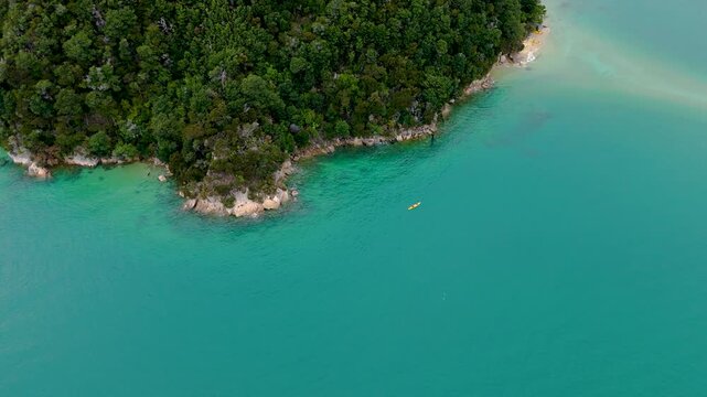 Aerial view of a lone kayak glides through turquoise waters near a lush forest, contrasting with the sandy shore, Abel Tasman National Park, New Zealand.
