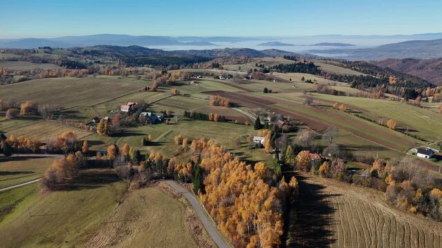 Aerial view of cultivated fields and scattered buildings with autumn foliage creating a patchwork of textures and colors, Detvianska Huta, Banska Bystrica Region, Slovakia.