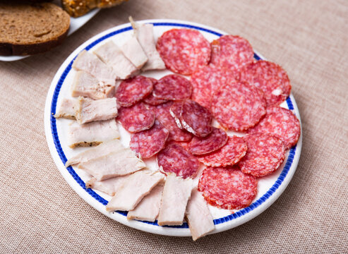 Slices of butifarra and smoked sausage dished up in a service plate on the laid restaurant table