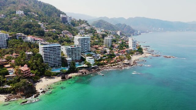 Aerial view of towering coastal condos meeting lush mountains, where turquoise waters crash against rocky shores, Puerto Vallarta, Jalisco, Mexico.