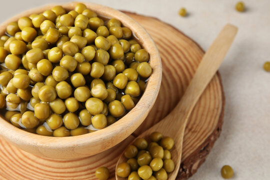 Wooden bowl and spoon with canned green peas on white background, closeup