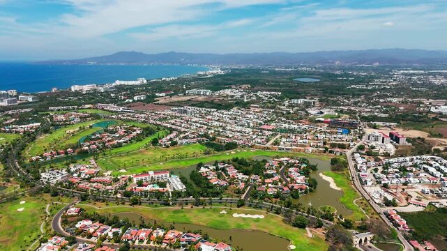 Aerial view of lush green golf courses intertwined with residential areas near the coast under a bright sky, Nuevo Nayarit, Nayarit, Mexico.