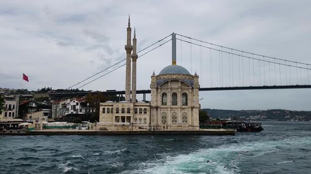 Scenic View of Iconic Ortakoy Mosque and 15 Temmuz Şehitler Bridge Over the Bosphorus Strait at Cloudy Day, Famous Istanbul Landmark Waterfront Architecture with Seagulls and Waves.