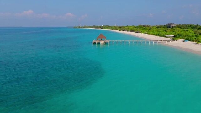 Aerial view of a wooden pier with a brown roof extending into the vibrant turquoise waters contrasting with the white sandy beach, Vashafaru, Thiladhunmathee Uthuruburi, Maldives.