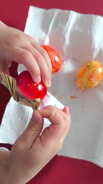 A child wraps an Easter egg in shiny gold foil to paint it gold.