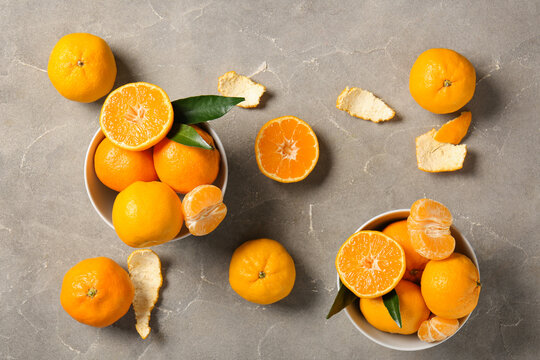 Bowls with sweet mandarins on grey background