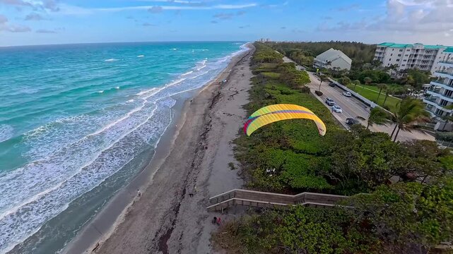 Aerial view of bright paraglider above the green vegetation, contrasted by the turquoise ocean and white sandy beach, Juno Beach, Florida, United States.