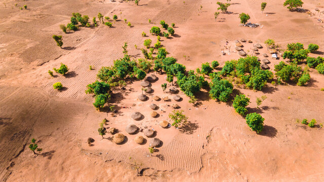 Aerial view of scattered round huts nestled amidst sparse trees and fields, casting long shadows on the ochre earth, Ouagadougou, Burkina Faso.