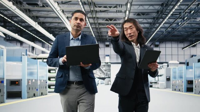 Multiracial management executives in microchip foundry brainstorming PCB components hardware fabrication steps. Senior manager and Indian man design semiconductors in manufacturing plant, camera A