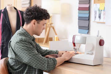 Obraz premium Young male tailor using sewing machine at table in atelier