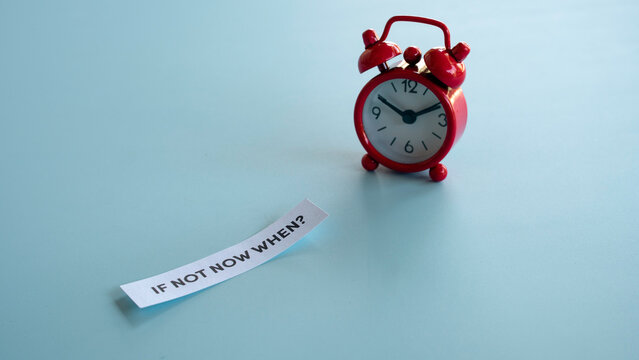 Red alarm clock with paper strip asking if not now when
