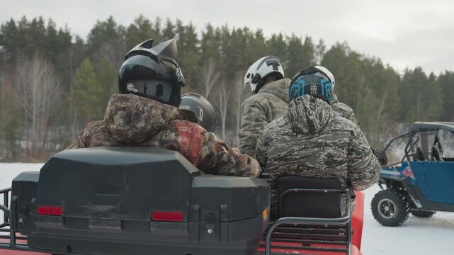 Two riders on atv rear seat in snowy forest, camo jackets and helmets, red utility atv rolling across frozen lake with UTV passing, rugged tires kicking snow, calm overcast light, anticipation