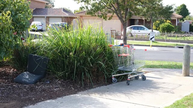 Abandoned shopping trolley and hard rubbish dumped beside a suburban street in Australia. Discarded items near residential houses and roadway in neighborhood. Illegal dumping, urban neglect issue