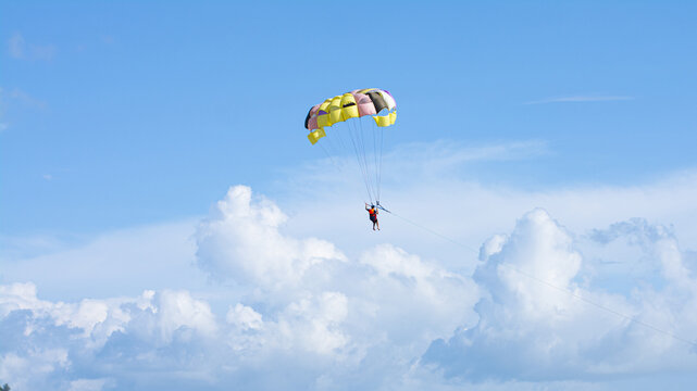 Cox's Bazar, Bangladesh - 18 August 2023: Aerial view of a parasailor suspended high above the fluffy white clouds, under a sunny azure sky, a dance of color and freedom.