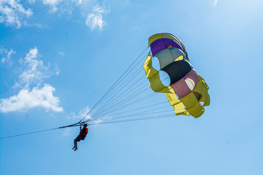 Cox's Bazar, Bangladesh - 18 August 2023: Aerial view of a vibrant yellow, purple, black, and white parasail gracefully soaring under a clear blue sky.