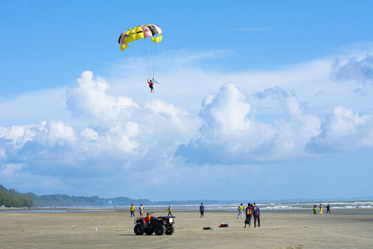 Cox's Bazar, Bangladesh - 18 August 2023: Aerial view of a vibrant parasail against the backdrop of the beach and the vast, blue sky, dotted with fluffy, white clouds.