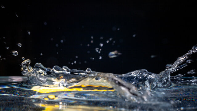 Water splashes from a surface as a yellow object is dropped into it at night