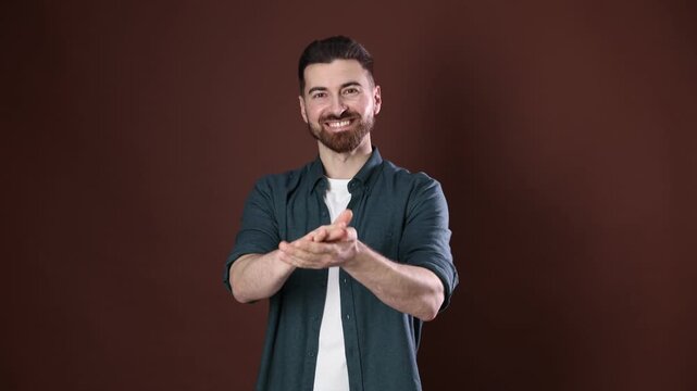 Positive man clapping hands on brown background