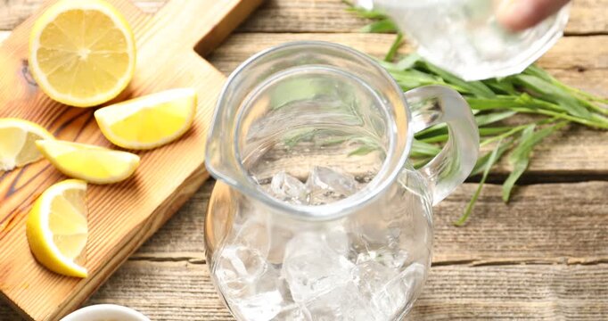 Woman making tasty lemonade with tarragon, ice cubes and lemon at wooden table, closeup