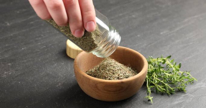 Woman putting dried thyme into bowl on black table, closeup