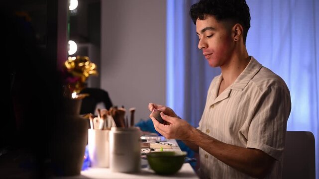 Young drag queen applying theatrical makeup in front of a mirror preparing for a show in a dressing room backstage