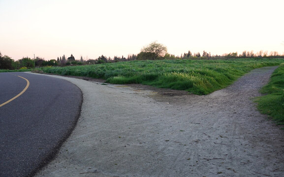 Fork in paved bike path and dirt trail at sunset representing choice and direction