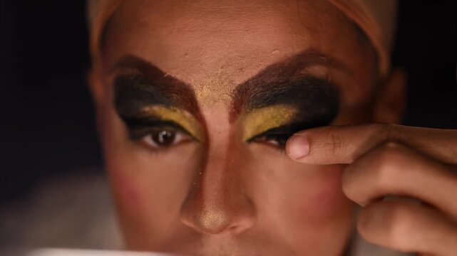 Drag queen artist applying false eyelashes and extravagant makeup getting ready for a performance in a dressing room backstage