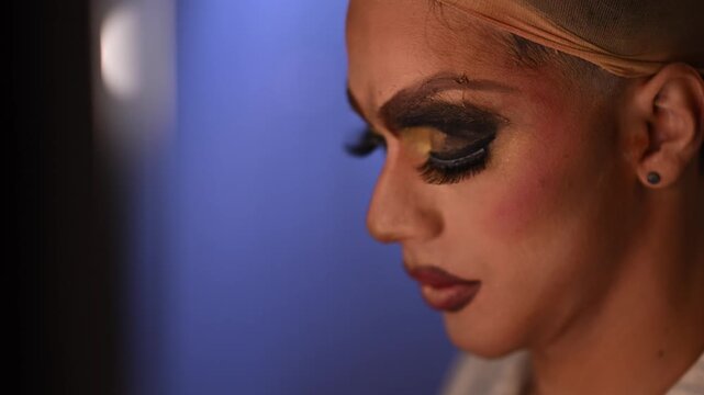 Closeup of a drag queen with elaborate makeup, including dramatic eyeliner, false lashes, and glitter, getting ready for a performance