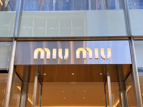 Miu Miu luxury fashion boutique illuminated logo and architectural exterior storefront design on a modern glass facade shopping mall building - Osaka, Japan, October 15, 2024