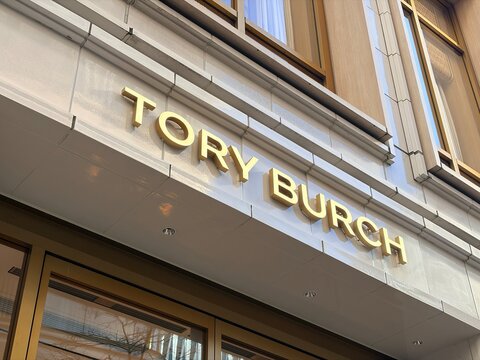 Tory Burch luxury fashion boutique exterior with gold brass logo lettering on white tiled facade of the Shinsaibashi flagship store - Osaka, Japan, November 12, 2024