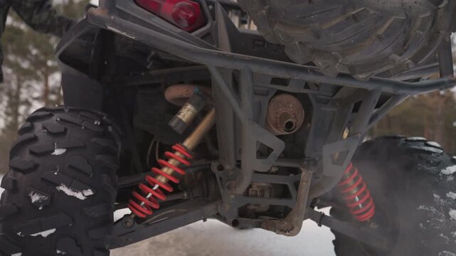 Atv rear suspension in snow, red coil shocks steaming exhaust, undercarriage closeup with lowangle perspective, gritty cold atmosphere, mechanic inspecting throttle and traction