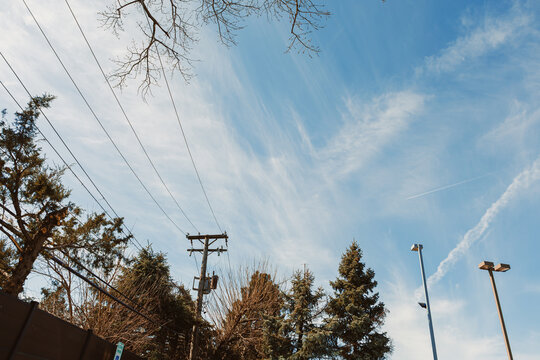 Clouds fill the sky over a city with trees, power lines, and street lights during the day in early spring