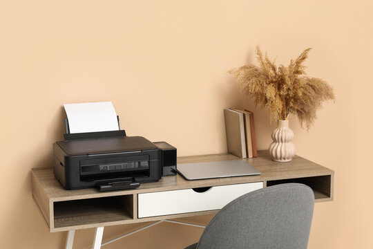 Modern printer and laptop on table near beige in home office