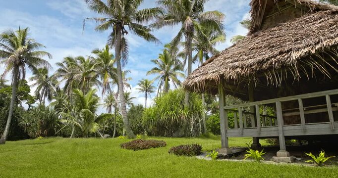 Thatched roof bungalow offering a peaceful retreat and relaxation, surrounded by a lush green lawn and abundant palm trees on tropical Port Resolution Tanna Island, Vanuatu. Travel, vacation, tourism