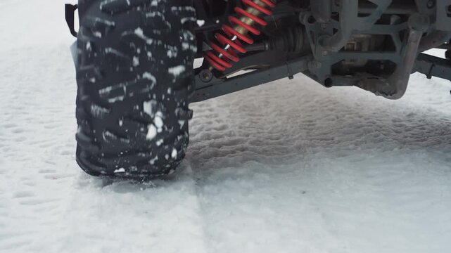 Closeup atv tires and suspension gripping snowy trail suspension compressing as wheel bites into powder, red coil springs and rugged undercarriage coated with snow, textured tread and rubber detail