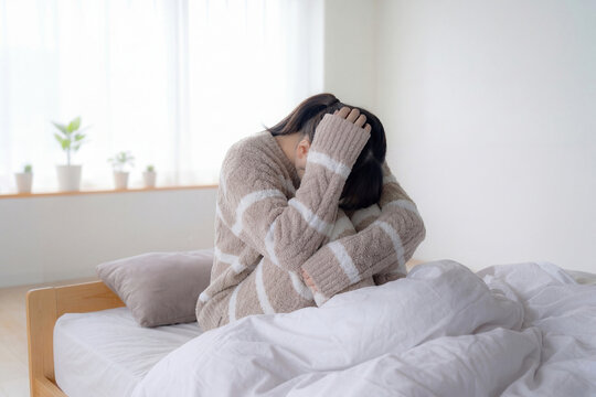 ベッドの上で女性が頭を抱えて座り込んでいるカット