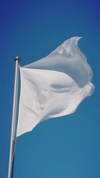 White flag gently waving on a flagpole against a clear blue sky. Available on 4K vertical video.