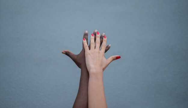 Manos de diferentes tonos de piel superpuestas simbolizando diversidad, inclusi&oacute;n y trabajo en equipo sobre fondo neutro