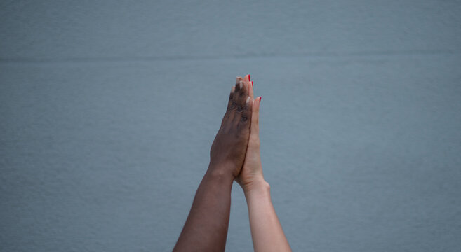 Manos de diferentes tonos de piel unidas en gesto de solidaridad y diversidad sobre fondo neutro