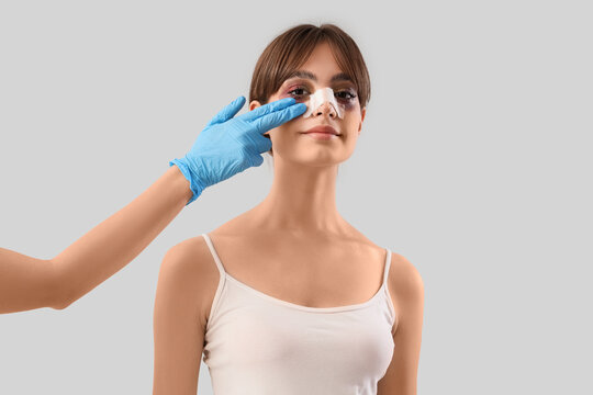Surgeon hand touching happy woman's bandaged nose after plastic surgery on grey background