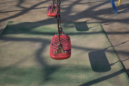 Red swing seat in empty playground with shadows