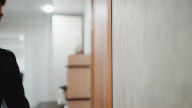 Caucasian grandson steps away from wooden doorway, boy glances back toward room with office chair soft overhead light and slow stride convey mix of relief and quiet longing, intimate family transition