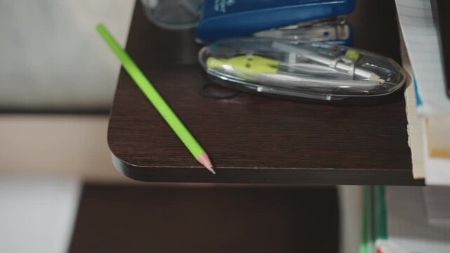 Grandson picks up fallen pencil from shelf and resumes drawing, small hand returns to sketching with green pencil, supplies and case visible, calm productive study and art moment.