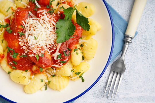 Plate of tasty gnocchi with tomato sauce and cheese on blue background