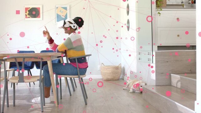 Vertical video: Reacting to overlay woman in sweater with AR visor tapping pink UI at dining table