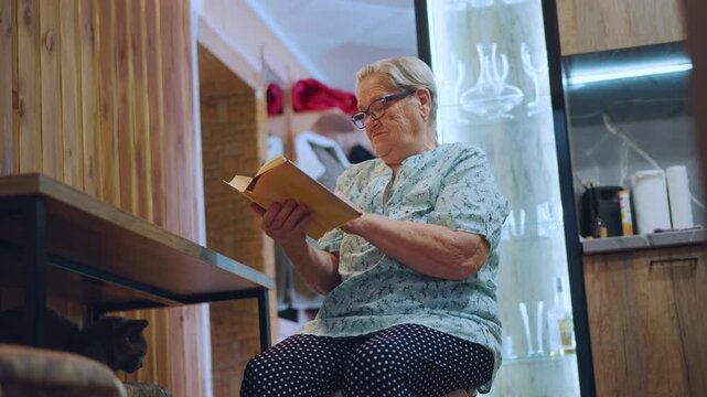 Grandma reading book in cozy corner, seated by wooden table with patterned skirt and spectacles, warm ambient light, intimate cafestyle kitchen backdrop, gentle focus on hands turning pages, nostalgic
