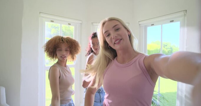 Diverse female friends recording for fun with blonde holding phone, singing, dancing by windows