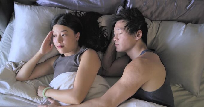 Woman rubbing eye and waking, man spooning, touching hair and green bangle for wellness on bed